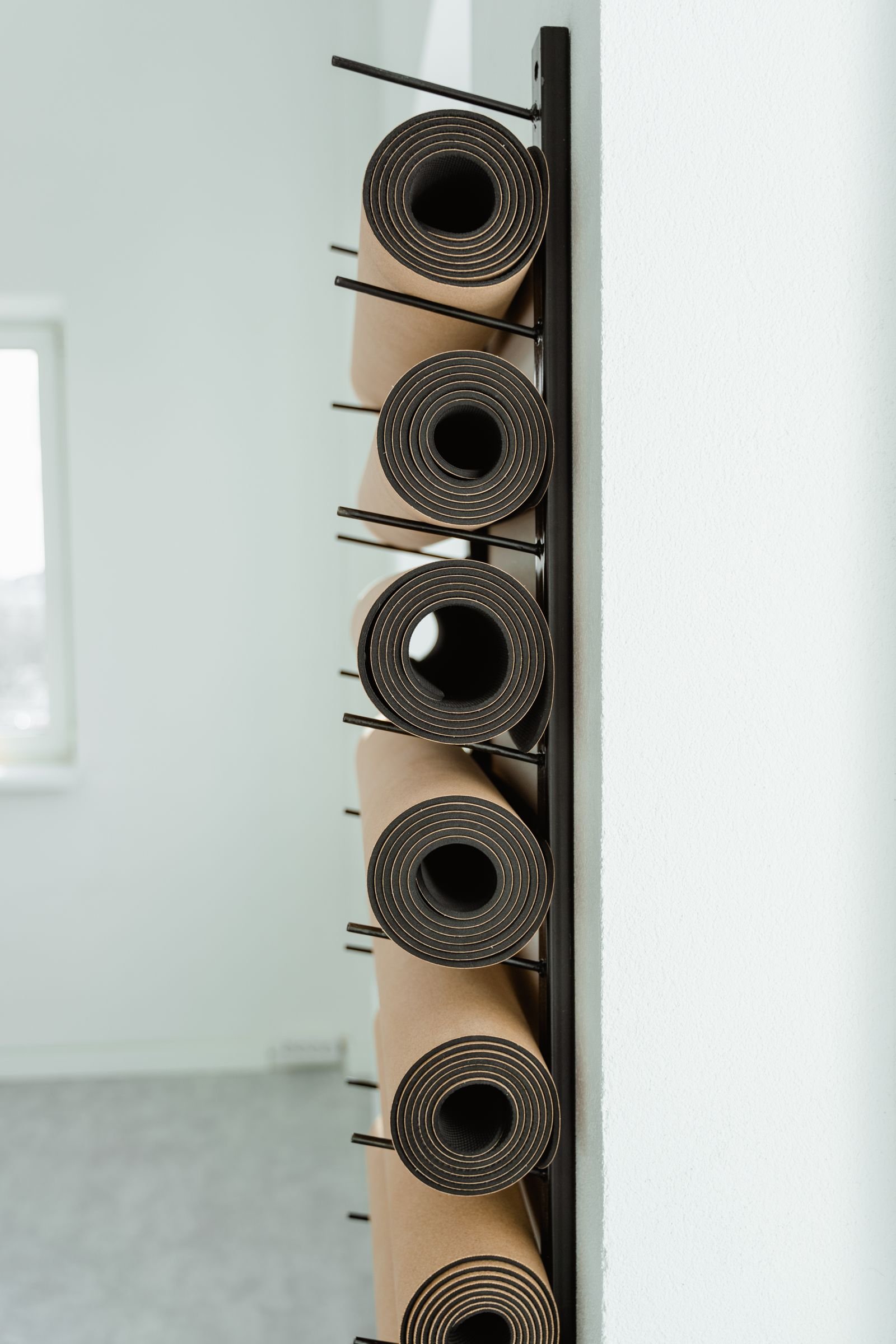 Rolled cork mats stored on a wall rack by the studio door